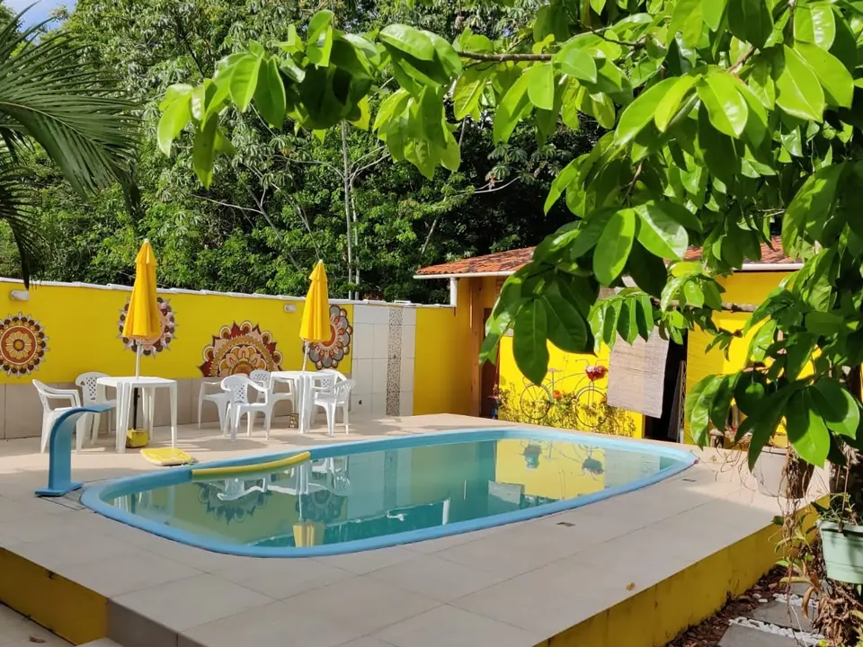 Piscina da pousada no jardim, com guarda-sóis amarelos e mandalas pintadas nos muros
